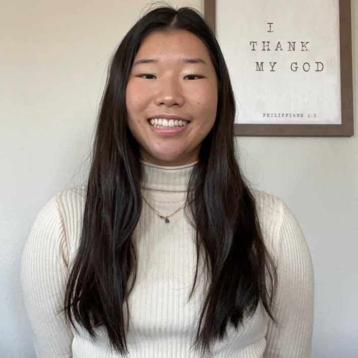Headshot of research assistant Andee in a white turtle neck long-sleeve with a photo frame reading bible verse I thank my God, Philippians 1:3 in the background