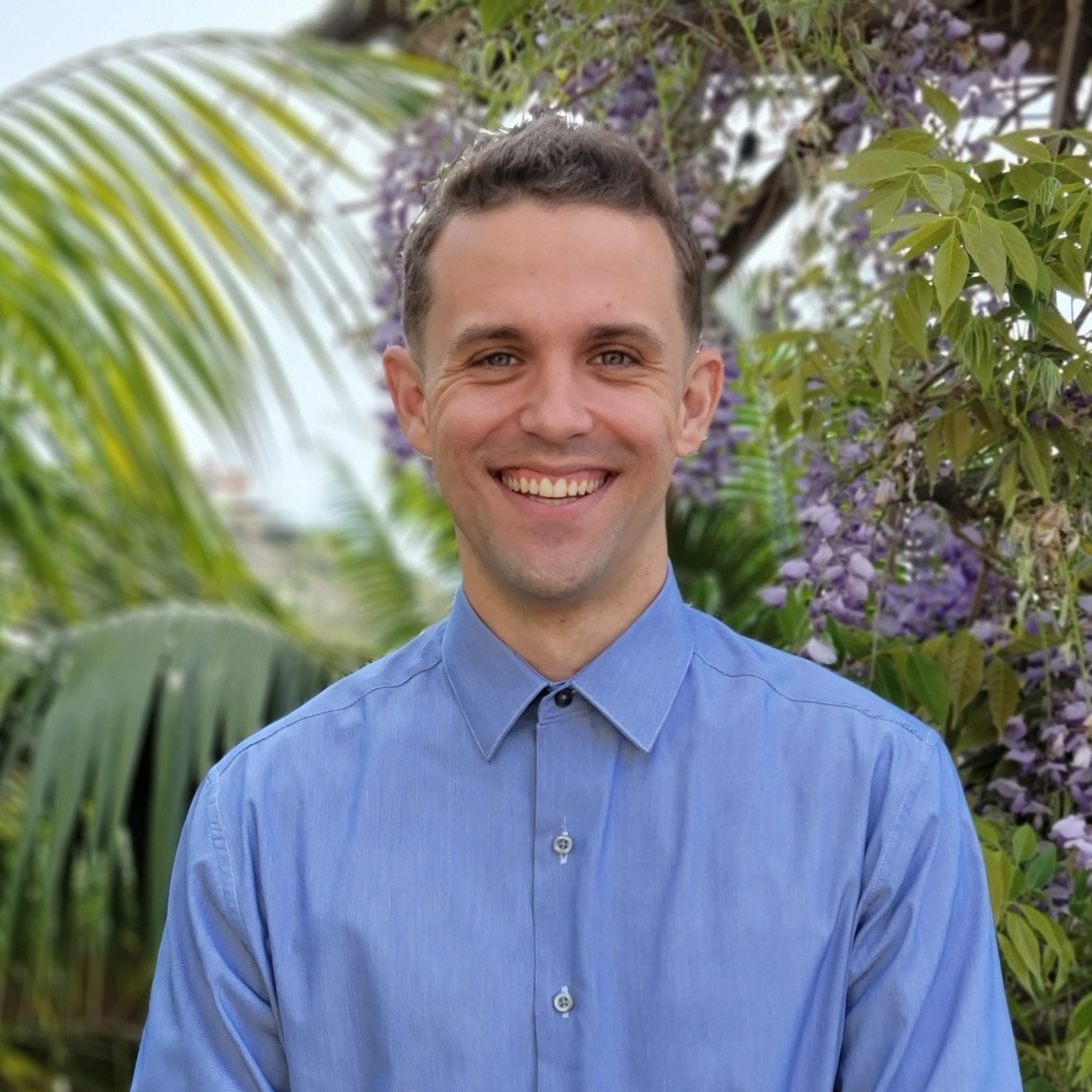 Headshot of former research assistant Casey in front of a palm leave and lavender bush background