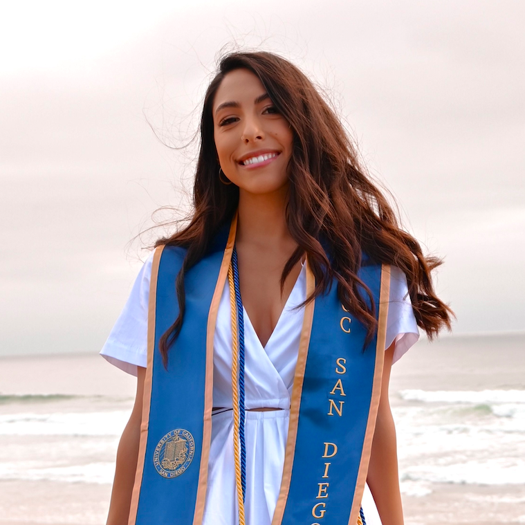 Headshot of former research assistant Cinthya wearing a blue and gold University of California, San Diego university stole on a beach