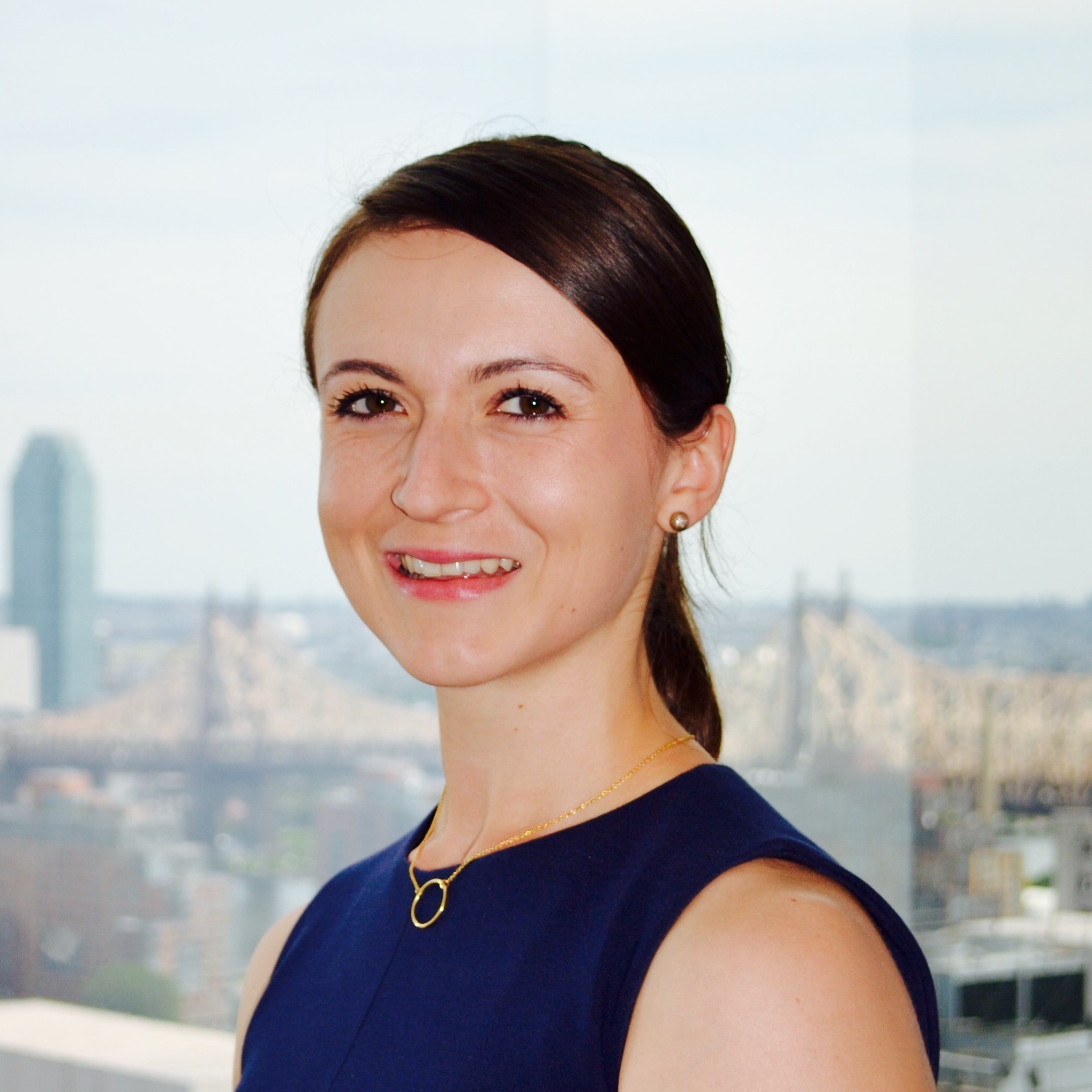 Headshot of former doctoral student Maria Kryza-Lacombe in front of a blurred bridge and skyscraper background