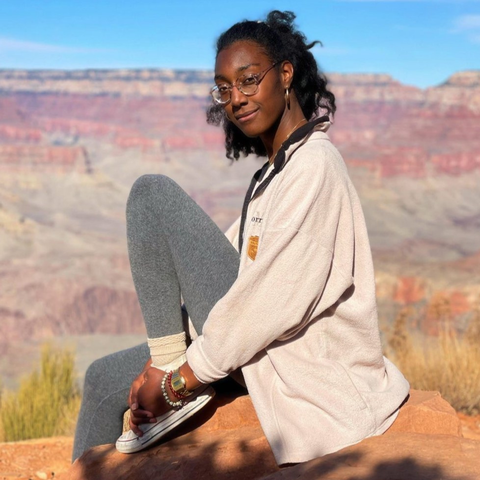 Former research assistant Nia sitting on a large red rock in front of a red desert hilly background