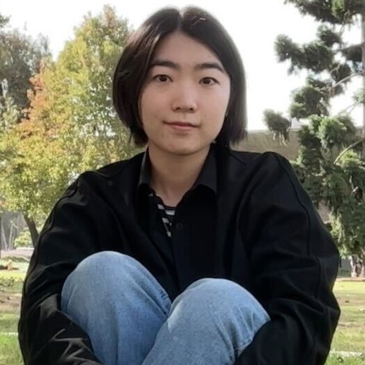 Ph.D. student Ruiyu sitting on grass with trees in the background and her legs crossed