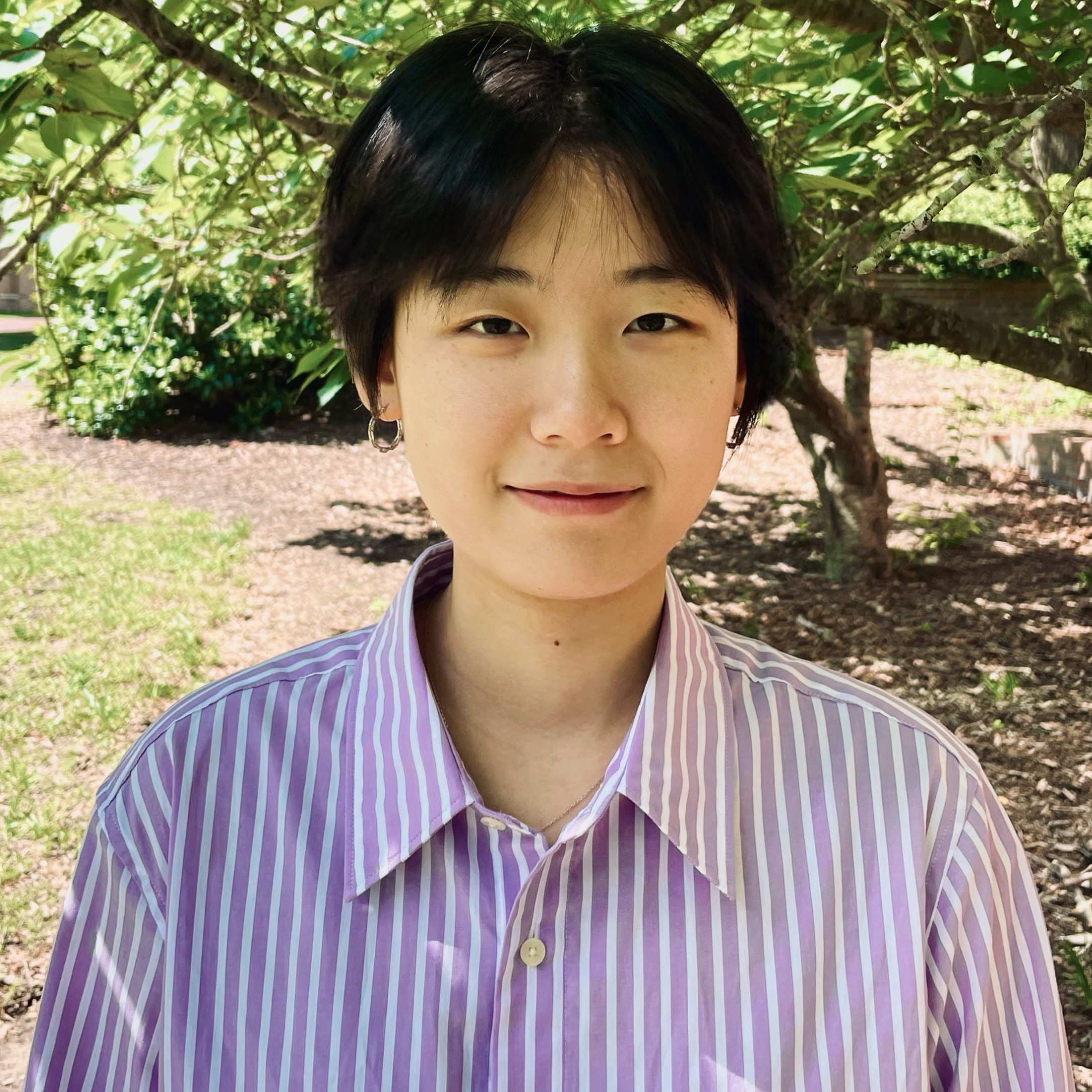 Headshot of Master's Student Yifan Yuan wearing a pink and white striped shirt and standing in front of a tree