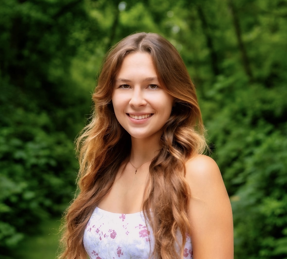 Headshot of Research Programmer Sophie Krivonosov wearing a floral top and standing in front of green foliage