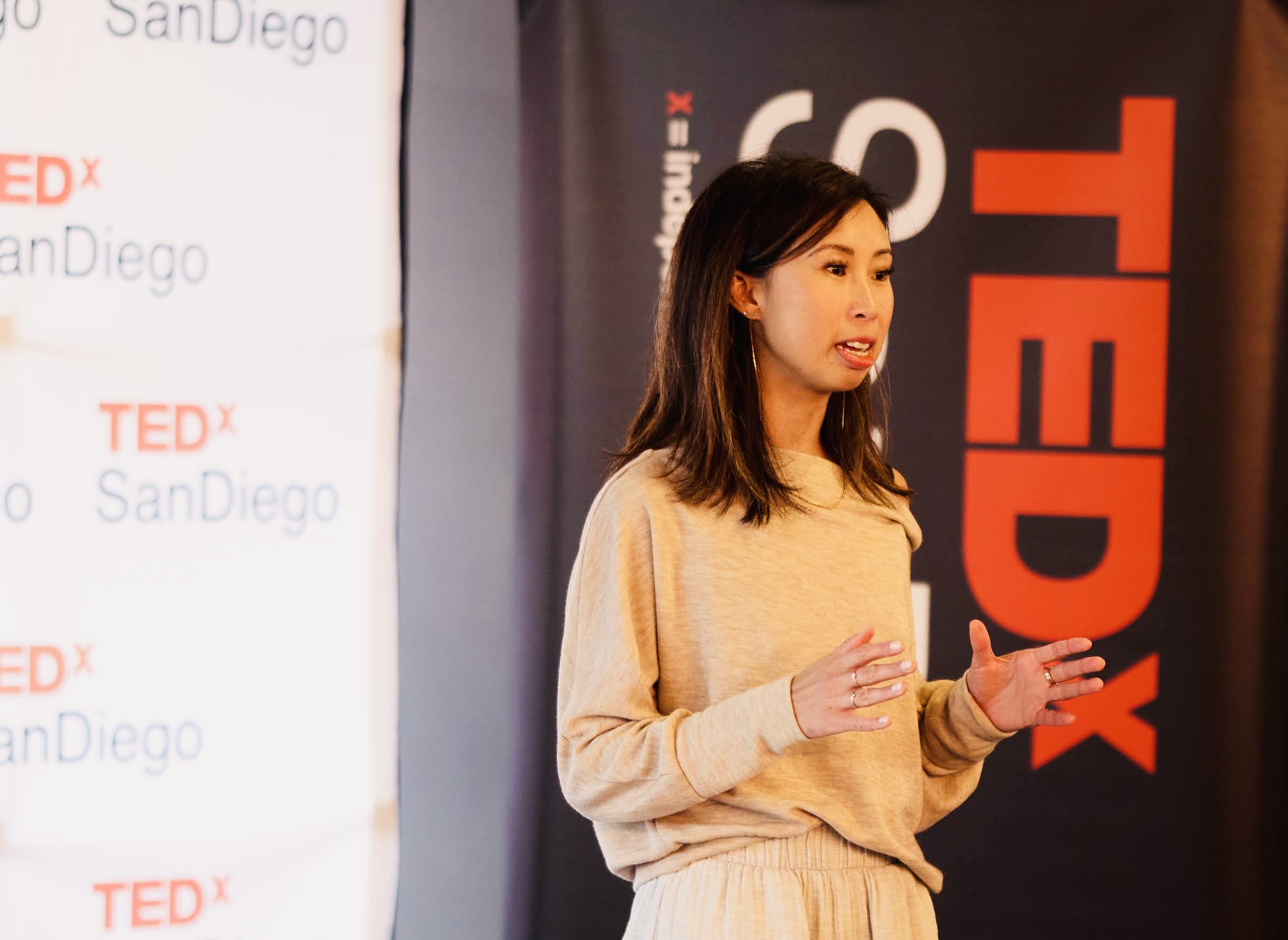 Image of Dr. Jillian Wiggins wearing a beige sweater and beige pants presenting in front of a TEDx background.