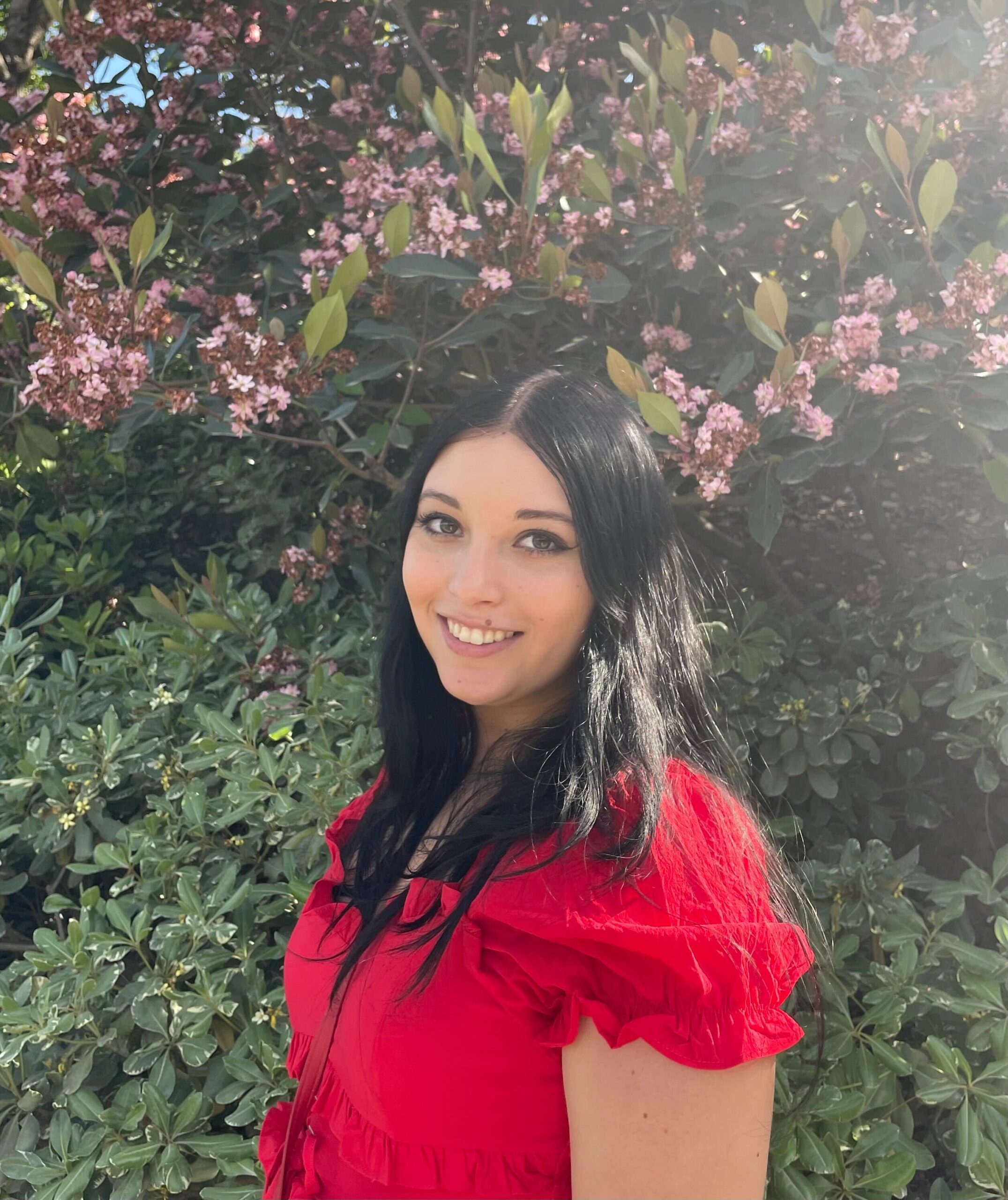 Headshot of Research Assistant Nicole Spiller wearing a red shirt and standing in front of green foliage.