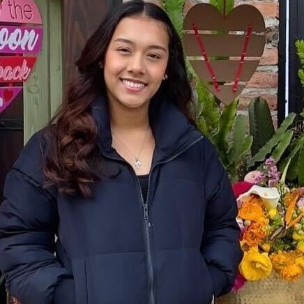 Headshot of research assistant Marissa Gutierrez wearing a black jacket in front of some greenery 