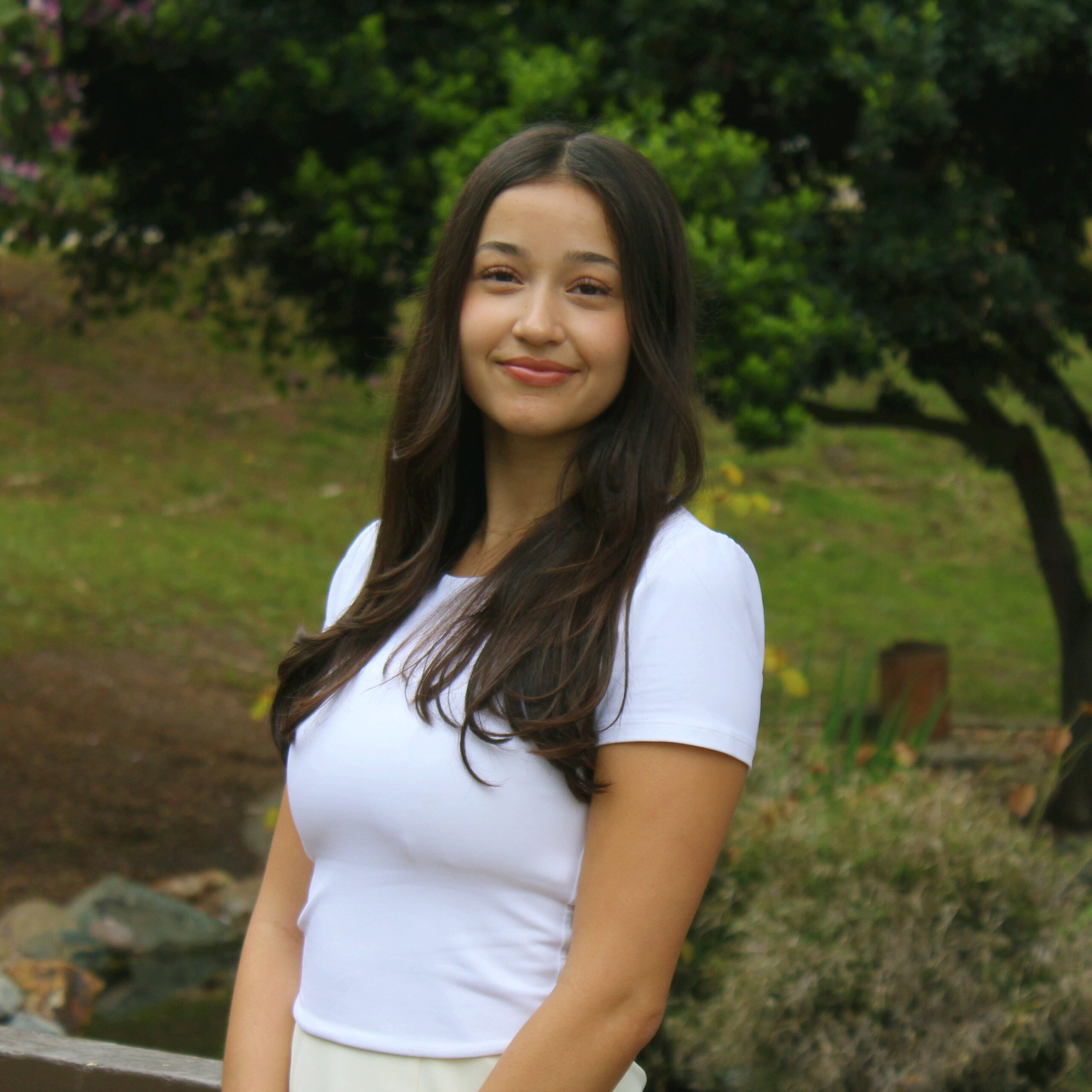 Headshot of research assistant Ashley Calbert smiling in a white t-shirt outside with some green foliage in the background.