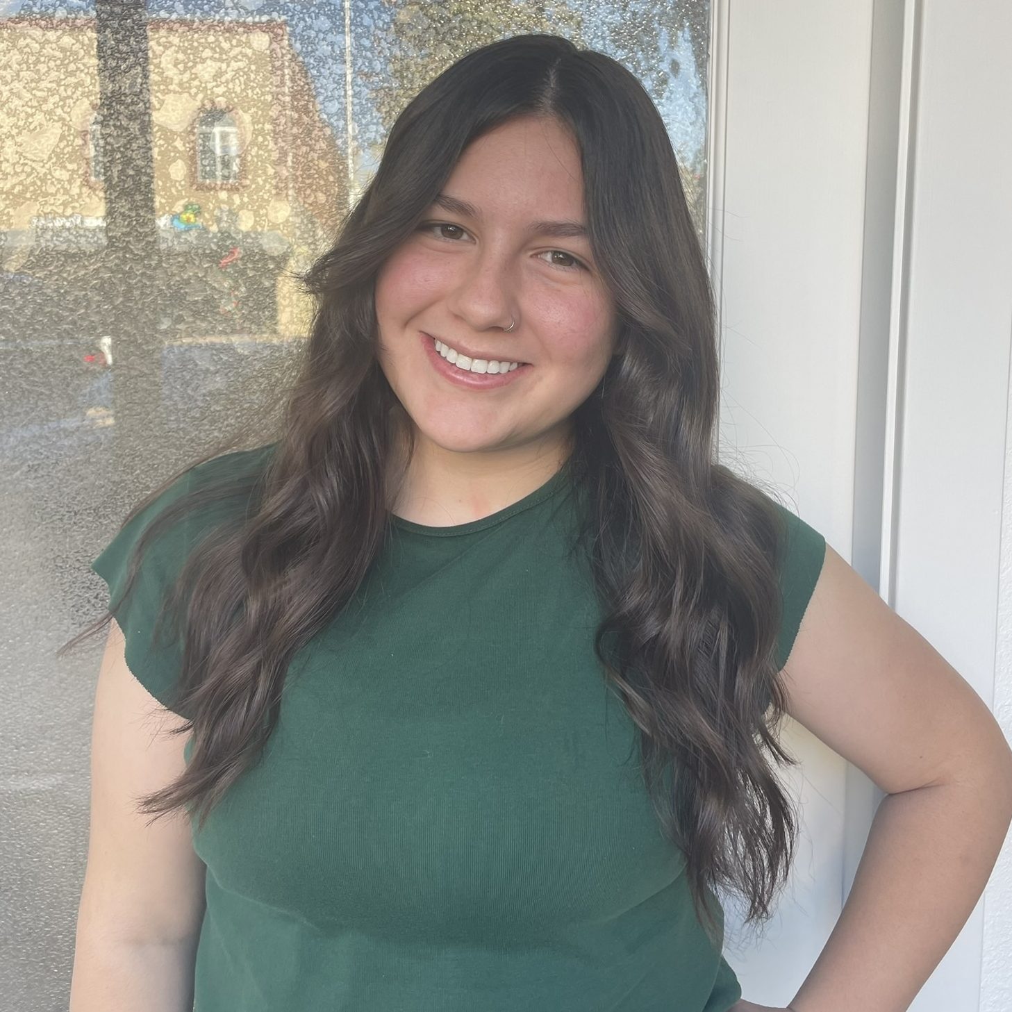 Headshot of Research Assistant, Victoria Medina, wearing green blouse standing outside with hand on hip