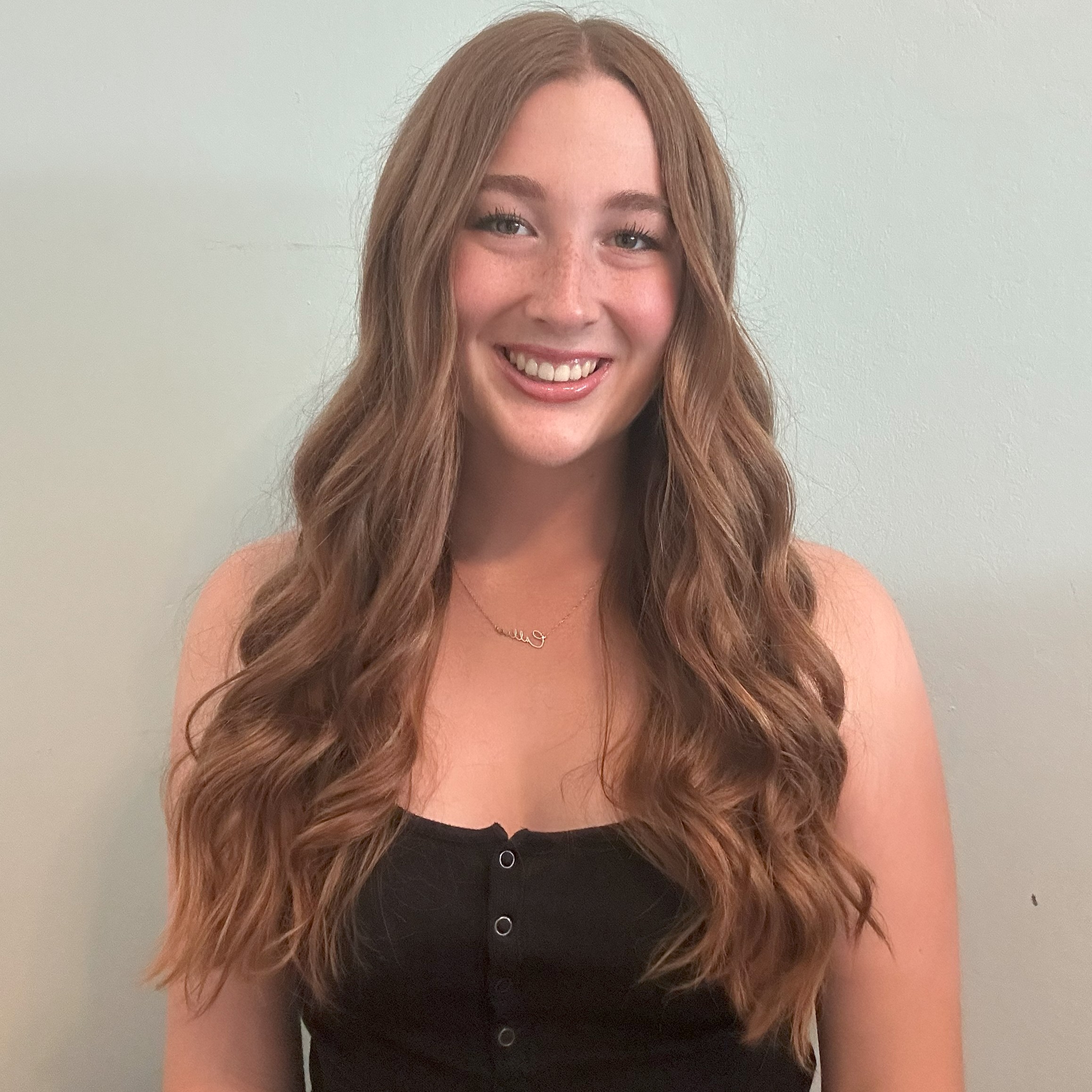 Headshot of research assistant, Callie Watson, in front of a white wall and wearing a black shirt with their hair down smiling