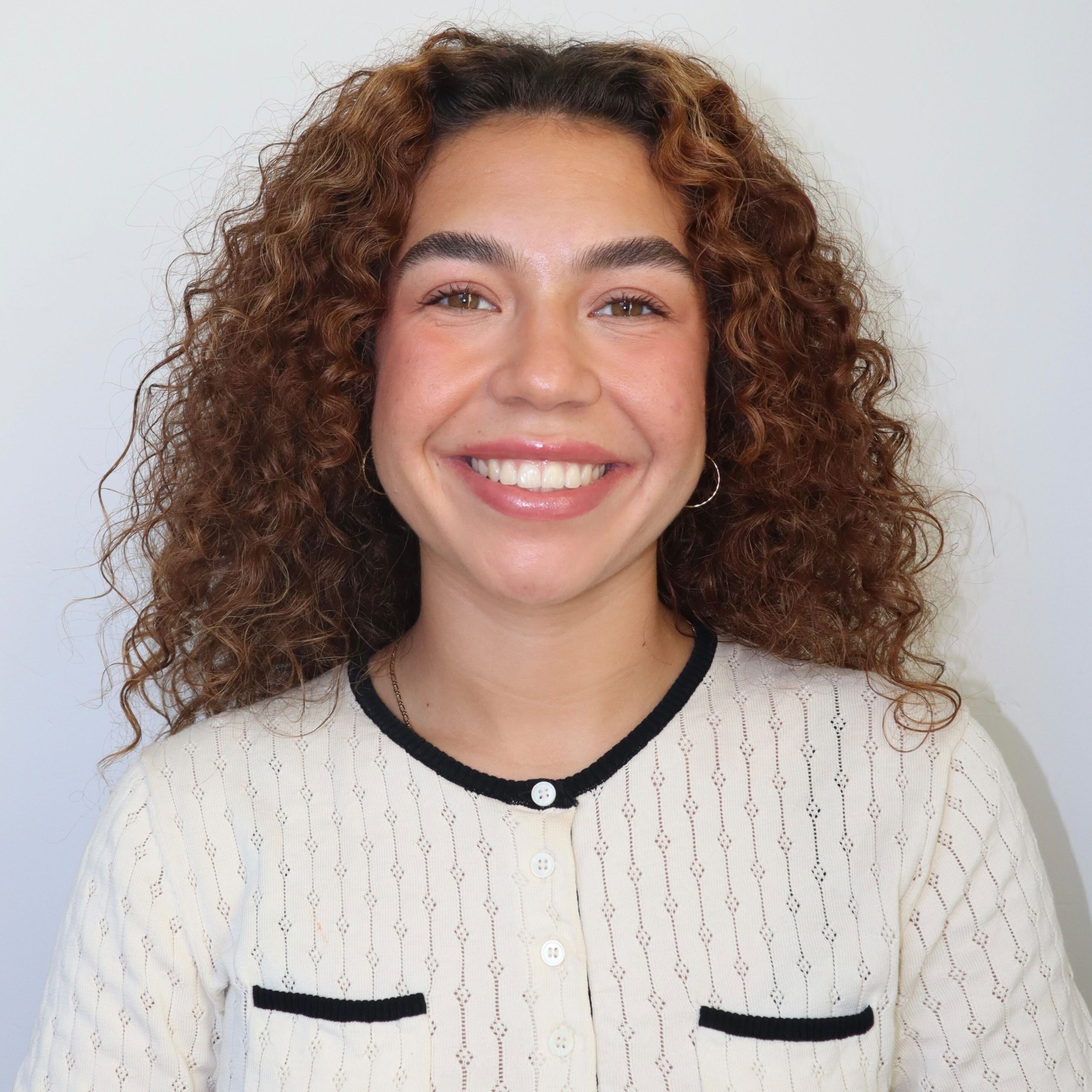 Headshot of research assistant, Rebecca Espat, smiling in front of a white wall with their hair down wearing a white button up
